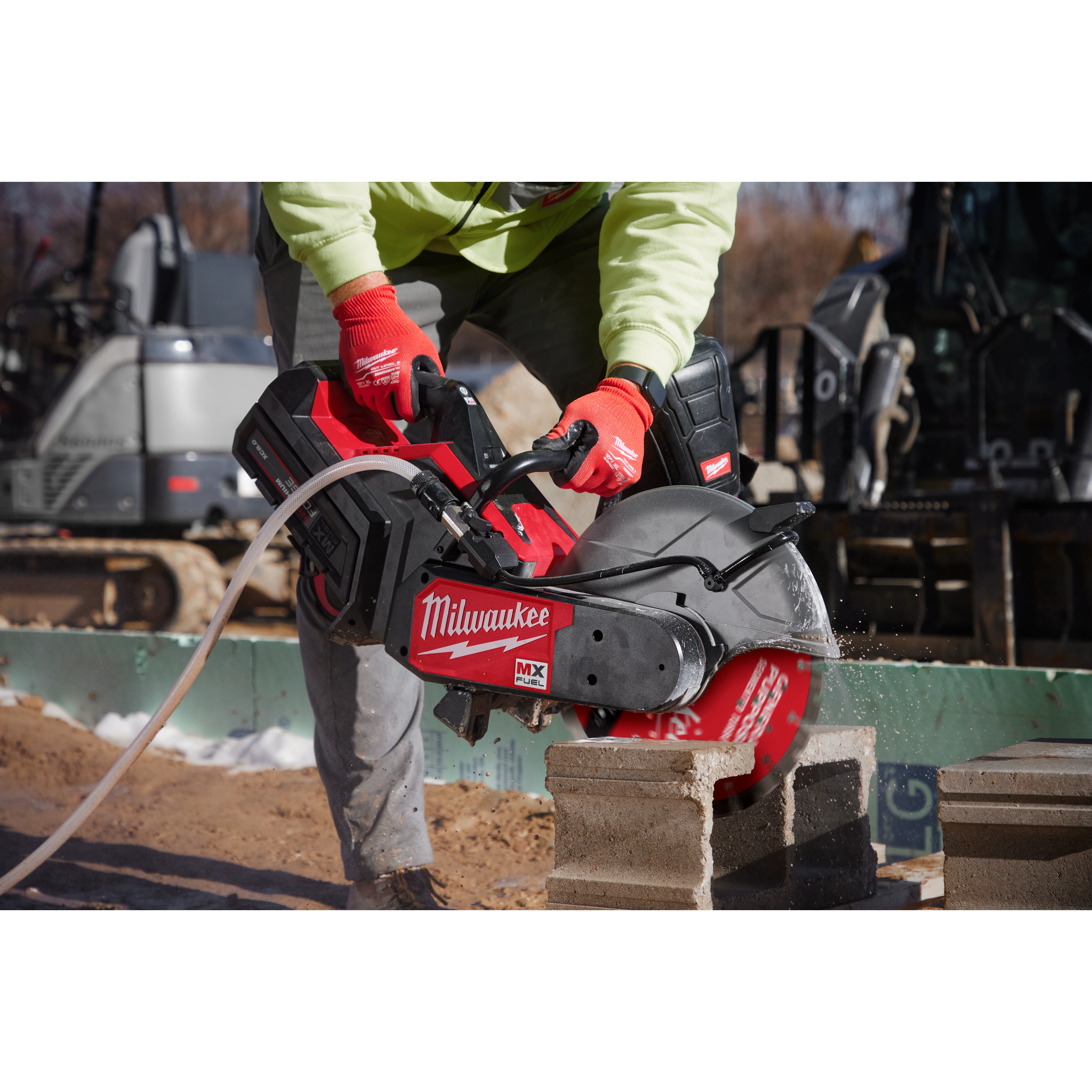 A person wearing a green jacket and red gloves uses a Milwaukee power saw with a 14" DIAMOND ULTRA™ Segmented Turbo, General Purpose Diamond Blade to cut concrete blocks on a construction site.